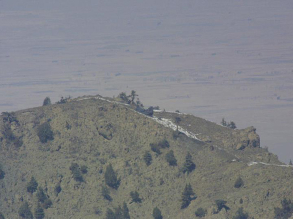 Imagen diurna del Chinook RAZOR1 en la cima de Takur Ghar tomada mirando la cara Oeste de la montaña. En la foto se ve justo a su izquierda una roca donde estaban unos búnkeres y n árbol con forma de bonsái